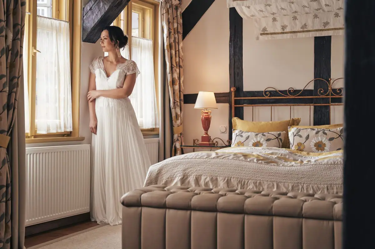 Hochzeitssuite Eine Frau in einem weißen Kleid steht in einem Schlafzimmer.