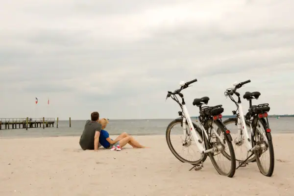 Ein Mann und eine Frau sitzen am Strand neben Fahrrädern.