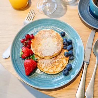 Frühstück am Gardasee Ein Teller mit Pfannkuchen, garniert mit Beeren, neben einer Tasse Kaffee.
