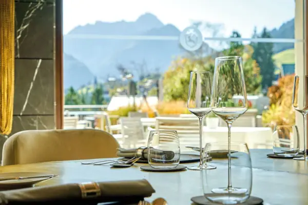 Ein Tisch mit Weingläsern und Besteck mit Blick auf eine berstliche Berglanschaft mit Bäumen durch ein Fenster im Hintergrund..