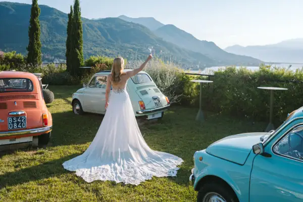 Empfang auf der Terrasse 500 Eine Frau im Hochzeitskleid hält ein Glas Champagner vor einem Fiat 500 Auto.