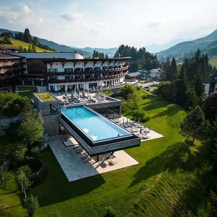 Ifen Hotel Kleinwalsertal Ein Outdoor Infinity Pool in einem Hotel, umgeben von Bäumen und einem klaren Himmel.