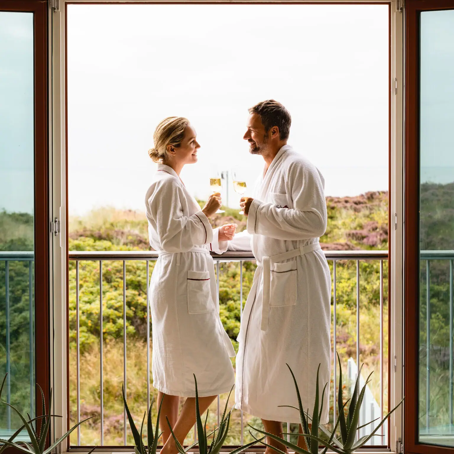 Pärchen im SPA Ein Mann und eine Frau in weißen Bademänteln stehen vor einem Balkon.