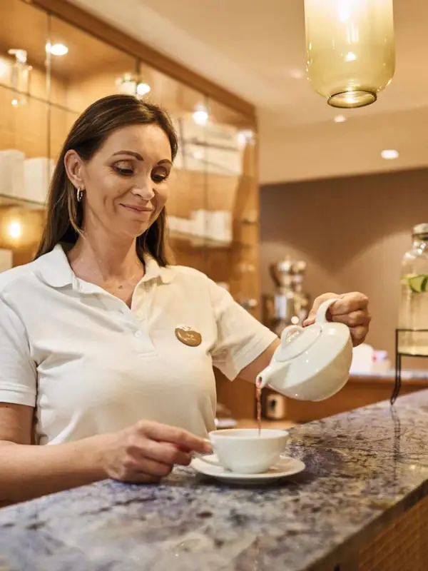Eine Frau an der SPA-Rezeption gießt Tee in eine Tasse.