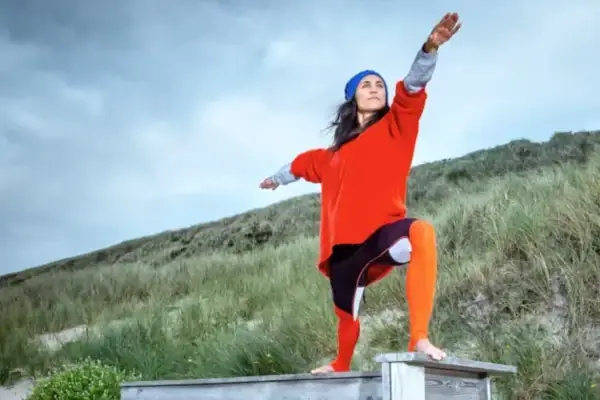 Eine Frau steht auf einer Bank in den Dünen in einer Yoga-Pose..
