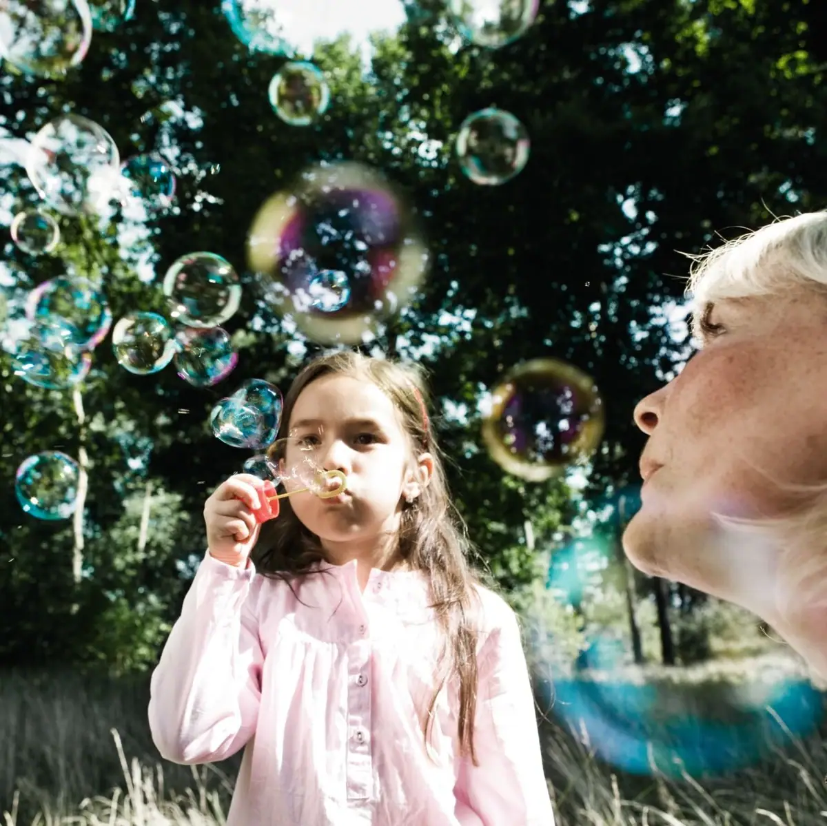 Eine Frau und ein Mädchen pusten Seifenblasen im Freien.