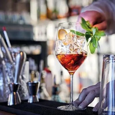 Bar 1.111 Ein Negroni auf Eis in einem Cocktailglas am Stiel dekoriert mit frischer Minze auf einem Bartresen.