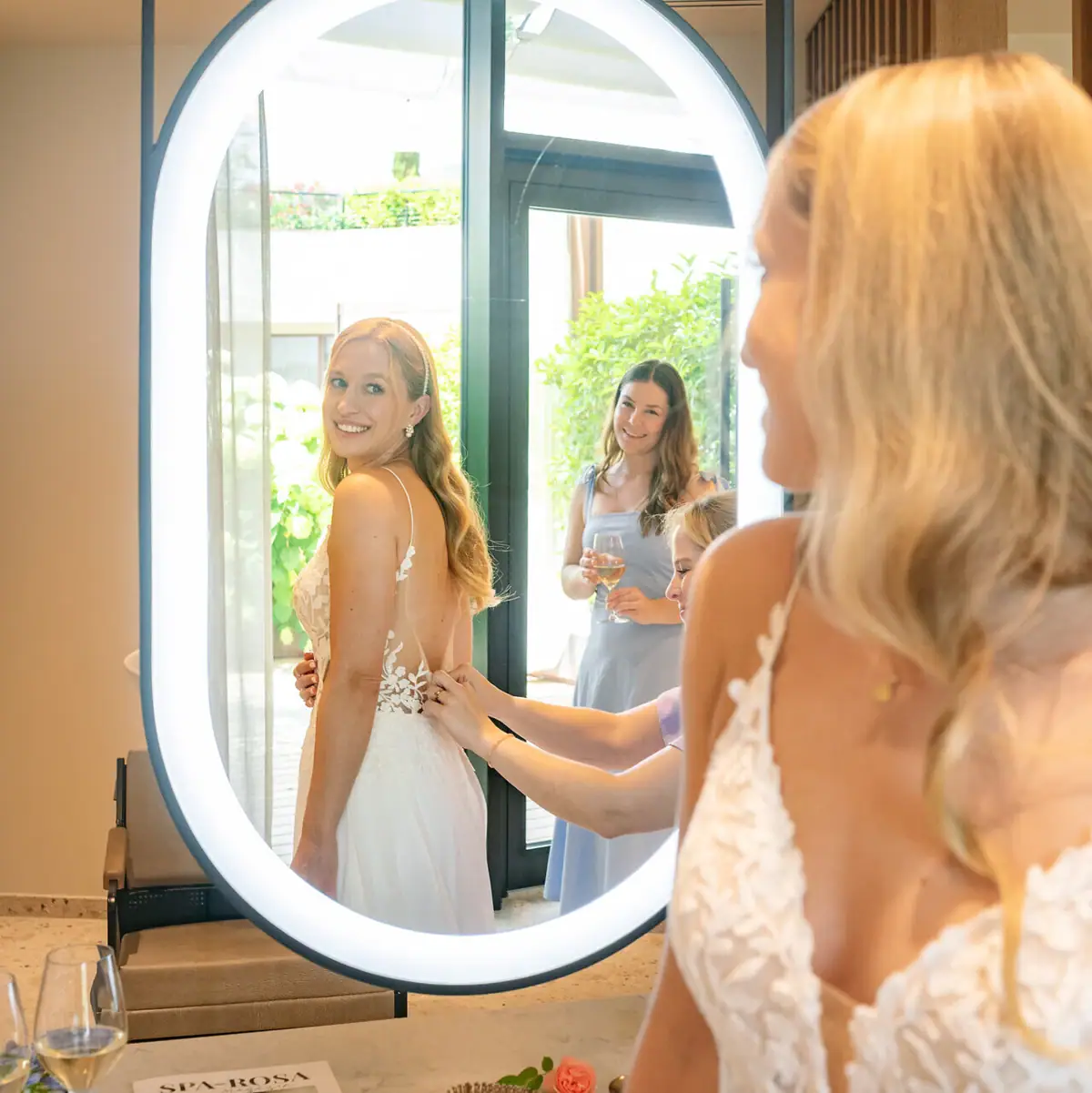 Getting Ready Moment im A-ROSA Gardasee Braut wird von Freundinnen beim Anziehen des Hochzeitskleids im A-ROSA Gardasee unterstützt.