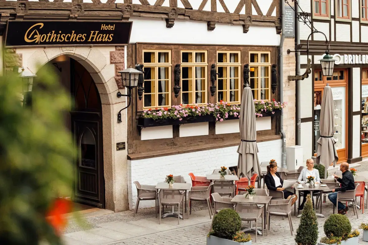 Eine Gruppe von Menschen sitzt an Tischen im Freien vor einem Gebäude.
