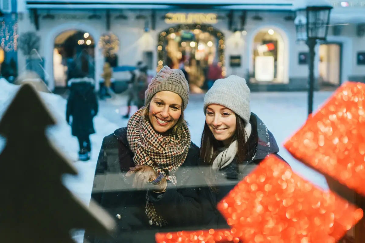 Shopping Zwei Frauen schauen lächelnd durch ein Fenster.