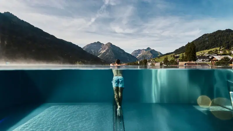 Ein Mann in einem Infinity Pool mit Bergen im Hintergrund.