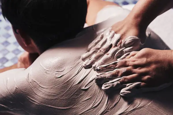 Hände tragen eine weiße Substanz auf den Rücken einer Person auf.