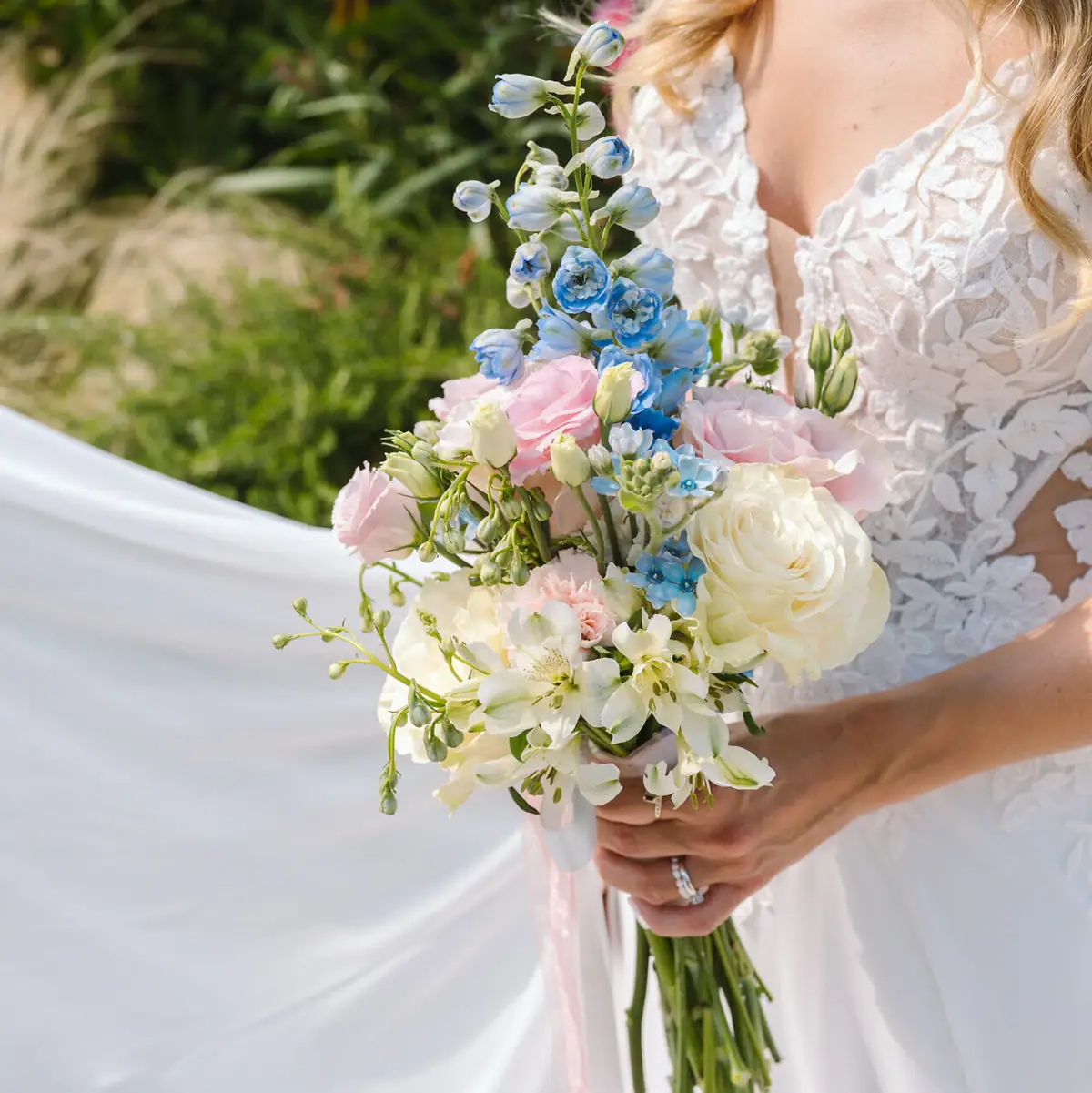 Blumenarrangement für den großen Tag Braut hält einen kunstvoll arrangierten Hochzeitsstrauß mit weißen, rosa und blauen Blumen.