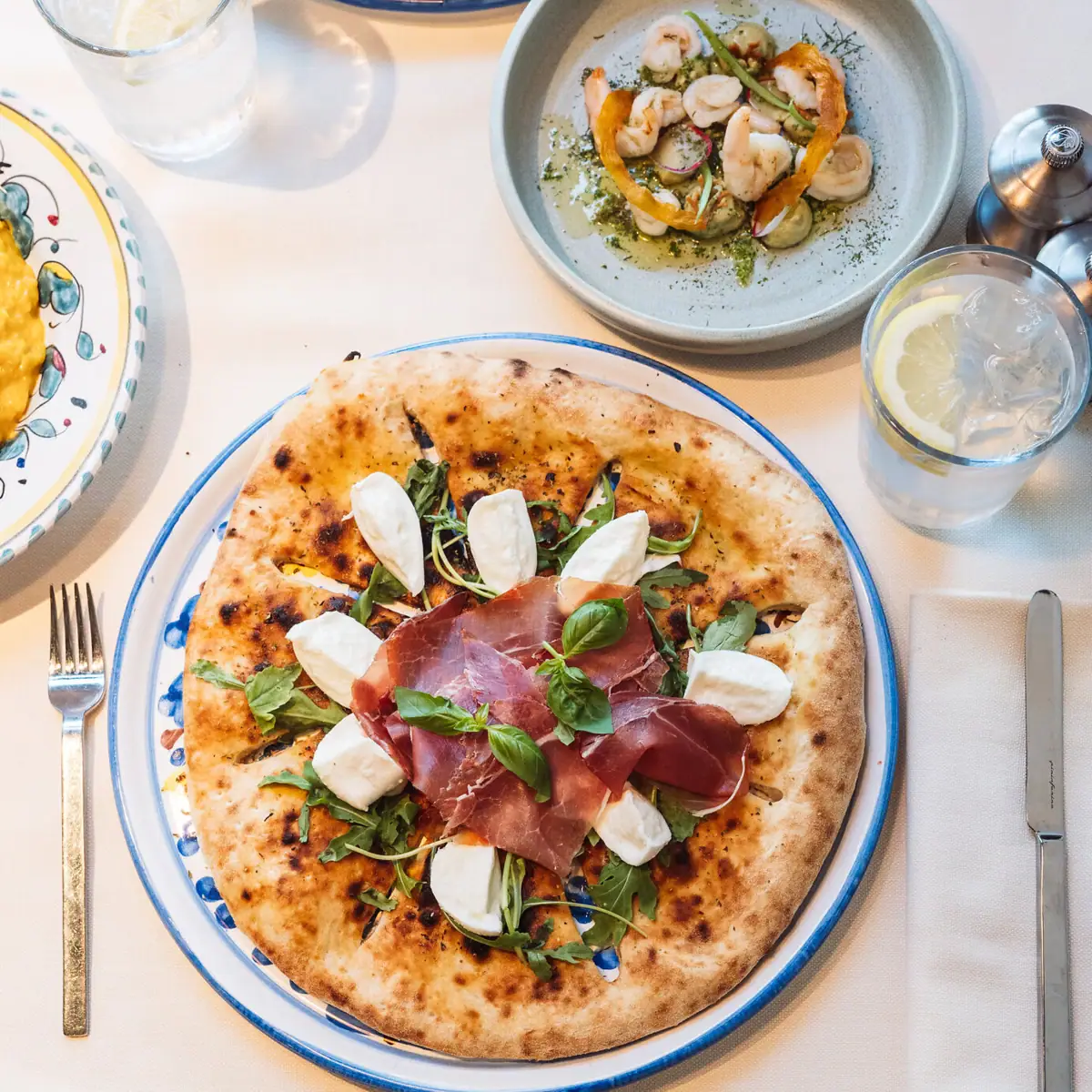 Kulinarik während der Tagung im A-ROSA Gardasee Ein Teller mit italienischer Pizza auf einem Tisch. Im Hintergrund sieht man ein Wasserglas sowie Scampi auf einem tiefen Teller.