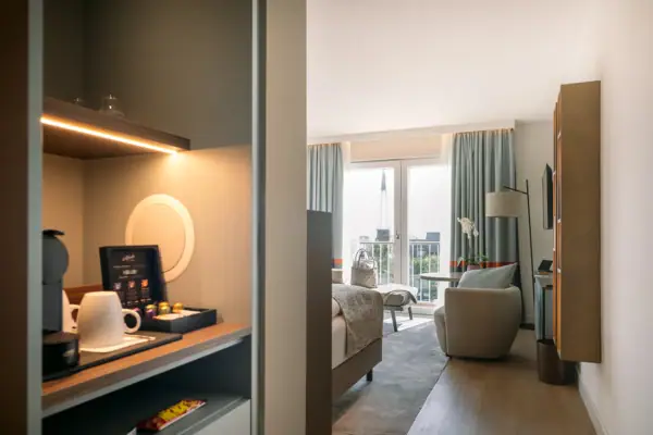 Zimmer A-ROSA Sylt Ein Hotelzimmer mit einer Kaffeemaschine, einem Sessel, großen Fenstern, einem Fernseher und einem Bett.