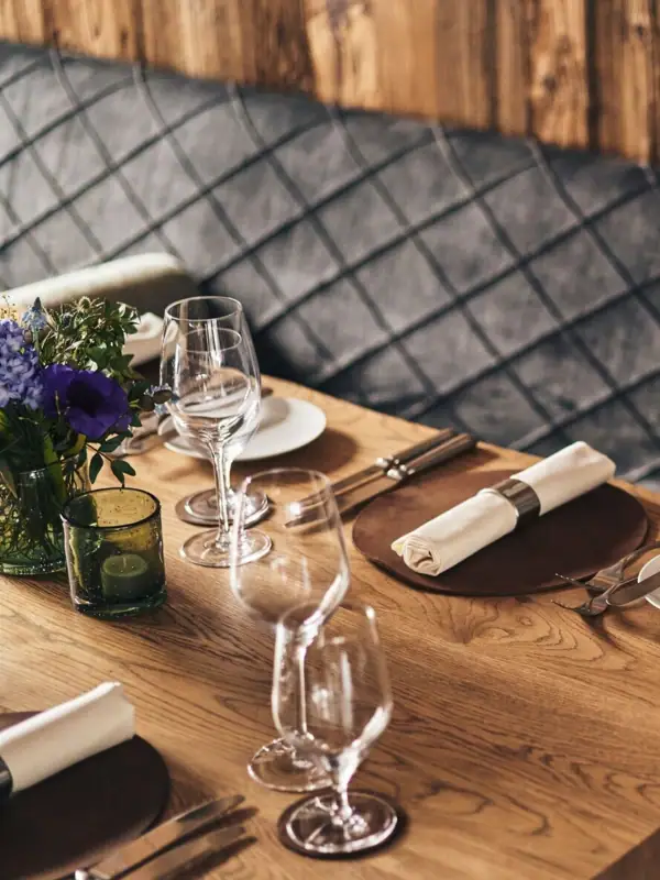 Ein Tisch mit Geschirr, Weingläsern und einer Vase mit Blumen vor einer Holzwand.