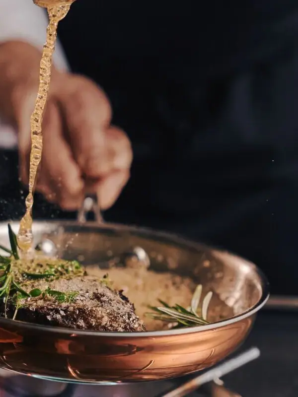 Eine Person gießt Flüssigkeit in eine Pfanne mit Essen.
