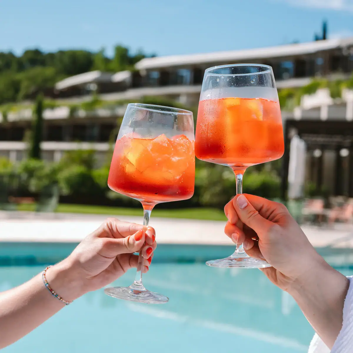 Cocktails an der Poolbar Ein Paar Hände hält Gläser mit Aperol und Eis gefüllt.