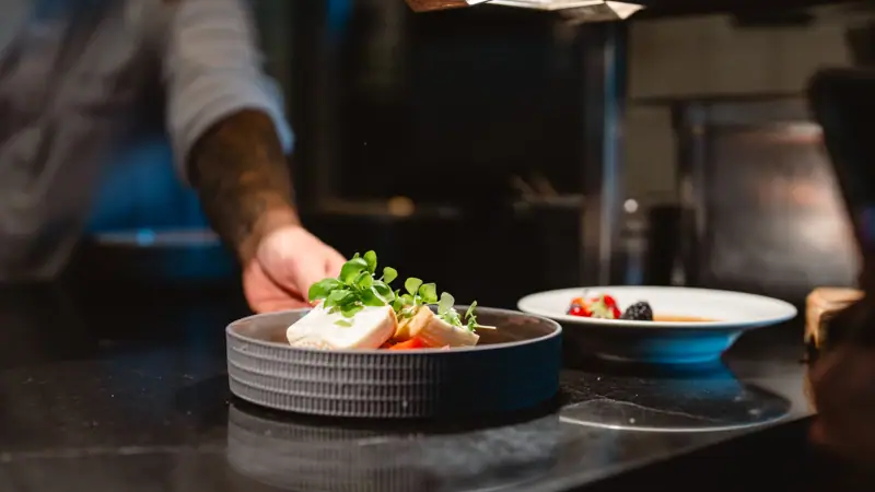 Tellerwerk Restaurant Eine Person hält Essen in einer Pfanne.