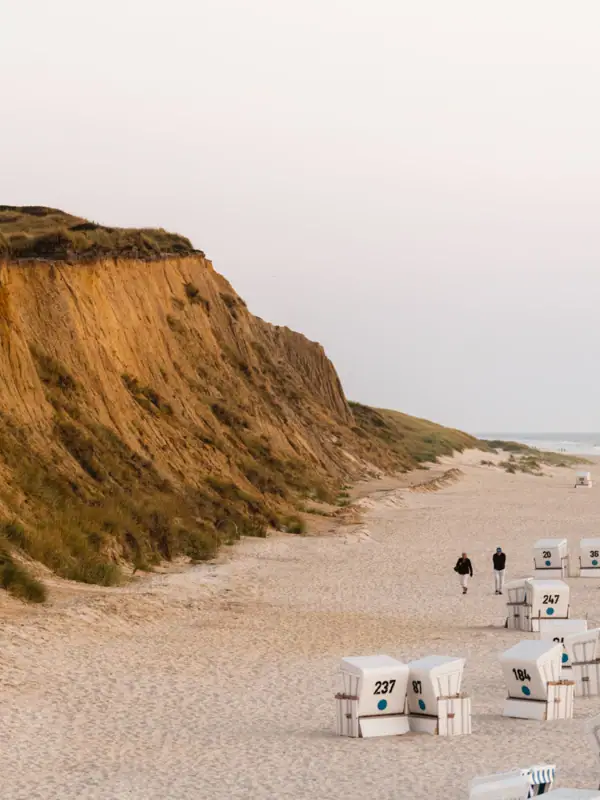 Strand mit weißen Stühlen und einer Klippe im Hintergrund.