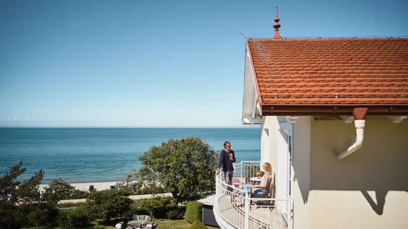 Ein Paar auf einem Balkon vom Ostseehotel mit Blick auf einen Strand.