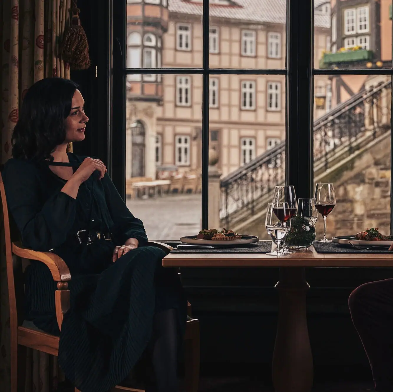 Ein Mann und eine Frau sitzen an einem Tisch mit Weingläsern vor einem Fenster.