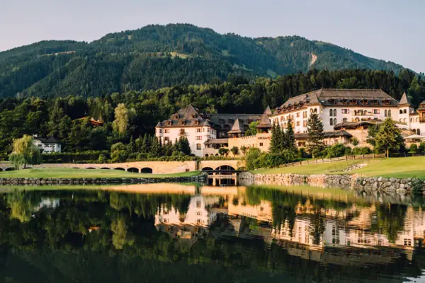 Ein Gebäude in der Nähe eines Sees mit Bäumen und Bergen im Hintergrund.