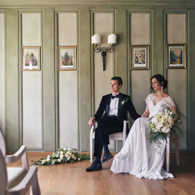 Hochzeitspaar Ein Mann und eine Frau sitzen in Stühlen, die Frau trägt ein Brautkleid und hält einen Blumenstrauß.