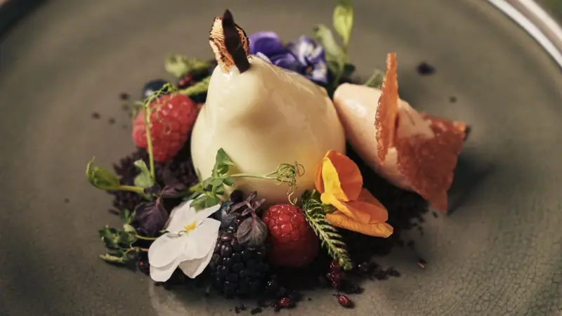 Ein Teller mit kunstvoll angerichtetem Essen, Obst und Blumen.