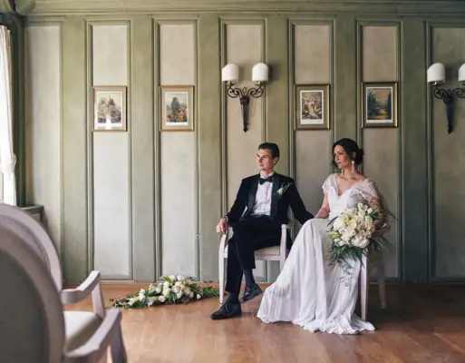 Ein Mann und eine Frau in Hochzeitskleidung sitzen auf Stühlen.