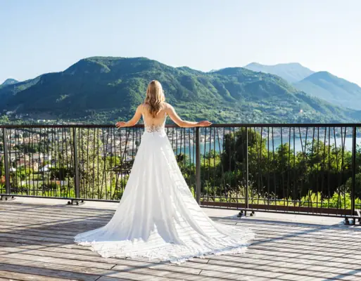 Hochzeit am Gardasee Eine Braut in einem weißen Kleid steht auf einem Balkon mit Blick auf den Gardasee.